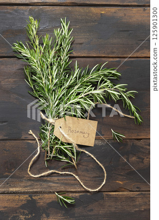 Fresh green rosemary sprigs with kraft paper text label dark weathered wooden table top view 125901300