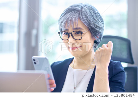 Senior business woman at desk work operating a smartphone in the office Senior business woman at desk work operating a smartphone in the office 125901494