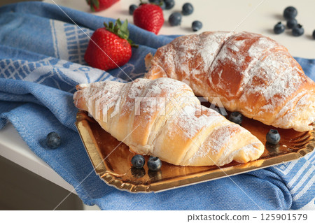Croissant, brioche bun with powdered sugar and berries on blue linen napkin. Breakfast and food. Croissant, brioche bun with powdered sugar and berries on blue linen napkin. Breakfast and food. 125901579