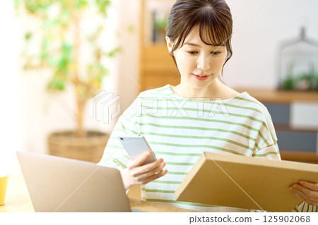 A young woman with a smartphone checking the luggage of the mail service in the living room A young woman with a smartphone checking the luggage of the mail service in the living room 125902068