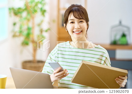 A young woman with a smartphone checking the luggage of the mail service in the living room A young woman with a smartphone checking the luggage of the mail service in the living room 125902070