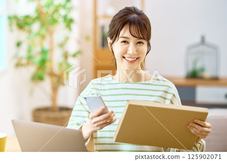 一位年輕女子拿著智能手機在客廳檢查郵件服務的行李 125902071