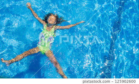 Child enjoys sunny day while floating in a swimming pool with clear blue water during summer Child enjoys sunny day while floating in a swimming pool with clear blue water during summer 125902600