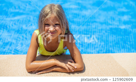 Young girl enjoying a sunny day at the pool, smiling with joy while leaning on the edge of the water 125902609