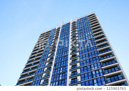 As I stand below, I gaze up at a tall building featuring blue windows As I stand below, I gaze up at a tall building featuring blue windows 125903763