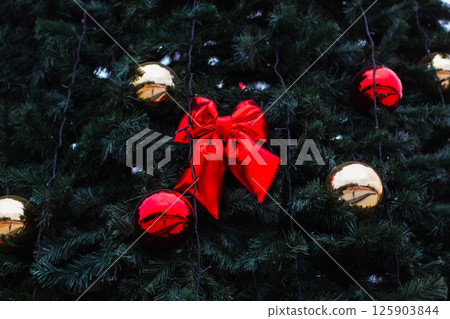 Close-up view of a beautifully decorated christmas tree featuring a vibrant red bow and shiny gold and red ornaments, creating an inviting, festive atmosphere perfect for the holiday season. Close-up view of a beautifully decorated christmas tree featuring a vibrant red bow and shiny gold and red ornaments, creating an inviting, festive atmosphere perfect for the holiday season. 125903844