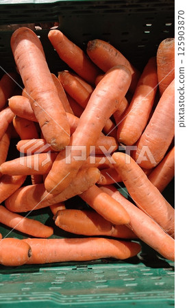 Fresh orange carrots piled in a green crate at a grocery store under bright lighting. Concept of healthy eating, organic vegetables and natural food market 125903870