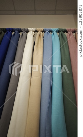 Assorted solid-colored fabrics hanging vertically in a row with soft lighting from above. Concept of textile selection, material quality and interior or fashion design resource 125903873