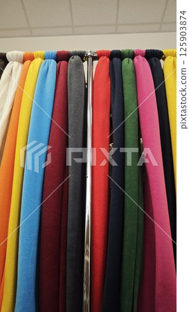 Bright fleece fabric rolls in multiple solid colors displayed on a rack in a fabric store. Concept of textile choice, warm material and vibrant design options for garments 125903874