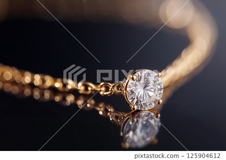 Elegant close-up of a shimmering diamond pendant in a quality gold setting, showcasing sophistication and luxury aesthetics, isolated on a dark background to emphasize its sparkle and brilliance. 125904612