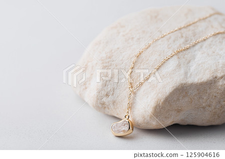 A delicate gold necklace with a polished gemstone pendant, showcased on a textured stone background. This luxury jewelry, perfect for fashion, showcasing minimalism and sophistication A delicate gold necklace with a polished gemstone pendant, showcased on a textured stone background. This luxury jewelry, perfect for fashion, showcasing minimalism and sophistication 125904616