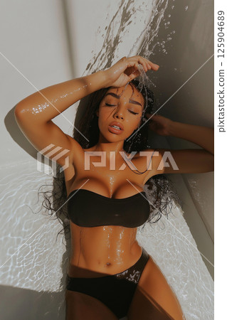 Elegant portrait of a woman under water flow with sparkling light effects. Yong woman enjoying water flowing with bright and natural lighting. 125904689