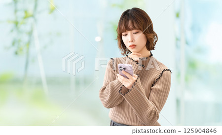 Woman/businesswoman thinking while looking at smartphone Woman/businesswoman thinking while looking at smartphone 125904846