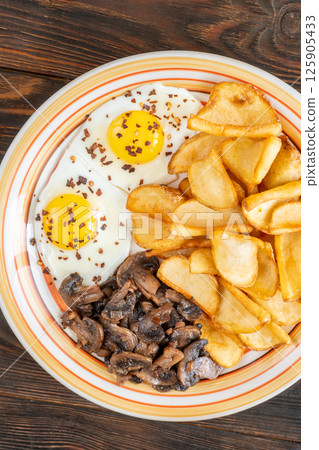 Golden potato dippers, fried eggs, and mushrooms on rustic textured table setting 125905433