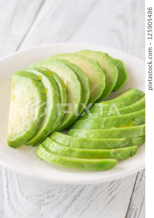 Ripe avocado sliced in white bowl, soft green curves catch natural light 125905486
