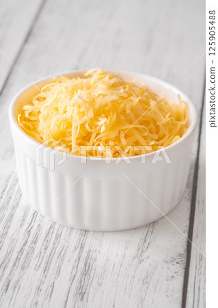 Finely grated cheddar cheese fills white bowl with vibrant golden orange shreds 125905488