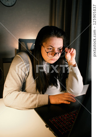 Young woman with eyeglasses working on laptop at home late at night, using modern technologies and getting online education. Remote learning concept. Online university. Focus on process. Young woman with eyeglasses working on laptop at home late at night, using modern technologies and getting online education. Remote learning concept. Online university. Focus on process. 125905837