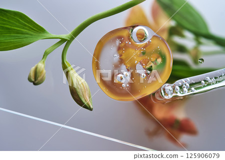 A pipette with a beautiful drop of serum on a background of lily flowers. 125906079