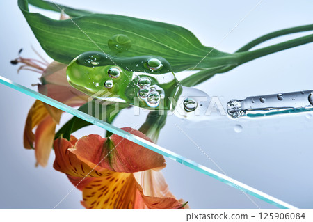A pipette with a beautiful drop of serum on a background of lily flowers. 125906084