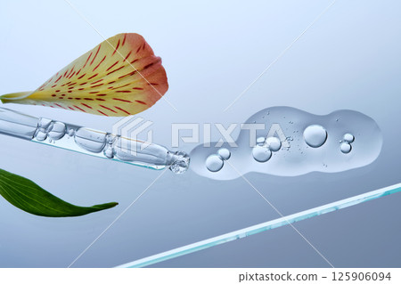 A pipette with a beautiful drop of serum on a background of lily flowers. 125906094