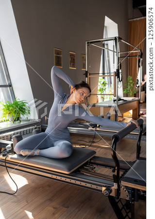 Woman training pilates on the reformer bed. Reformer pilates studio machine for fitness workouts in gym. Fit, healthy and strong authentical body. Fitness concept 125906574