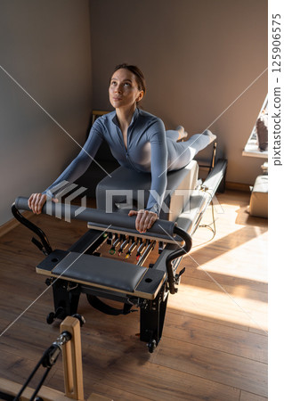 Woman doing Swan exercise on Pilates Reformer for the chest and back muscles, focusing on flexibility, strength, and control with determination Woman doing Swan exercise on Pilates Reformer for the chest and back muscles, focusing on flexibility, strength, and control with determination 125906575