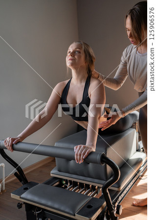 Woman doing Swan exercise on Pilates Reformer for the chest and back muscles, focusing on flexibility, strength, and control with determination 125906576