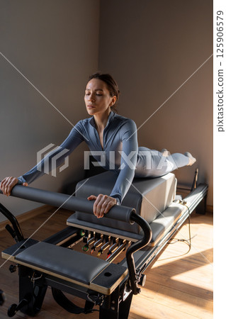Woman doing Swan exercise on Pilates Reformer for the chest and back muscles, focusing on flexibility, strength, and control with determination 125906579