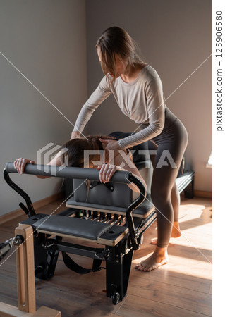 Woman doing Swan exercise on Pilates Reformer for the chest and back muscles, focusing on flexibility, strength, and control with determination 125906580