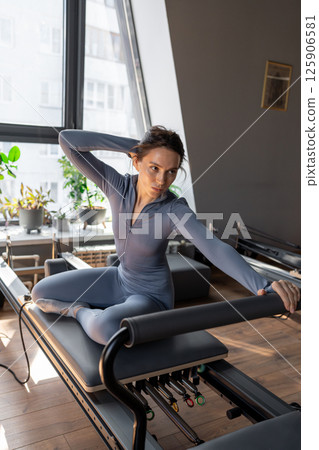 Woman doing mermaid exercise in a sunlite, modern pilates studio, embodying calm, focus, and strength. 125906581
