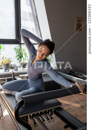 Woman training pilates on the reformer bed. Reformer pilates studio machine for fitness workouts in gym. Fit, healthy and strong authentical body. Fitness concept 125906583