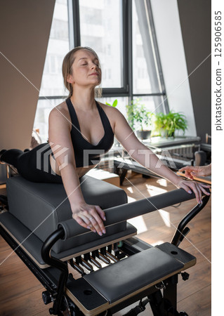 Woman doing Swan exercise on Pilates Reformer for the chest and back muscles, focusing on flexibility, strength, and control with determination 125906585