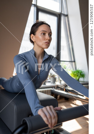 Woman doing Swan exercise on Pilates Reformer for the chest and back muscles, focusing on flexibility, strength, and control with determination 125906587