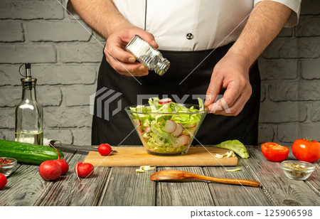 A chef mixes a vibrant salad using fresh ingredients like lettuce, radishes, cucumbers, and tomatoes, adding seasoning in a rustic kitchen environment A chef mixes a vibrant salad using fresh ingredients like lettuce, radishes, cucumbers, and tomatoes, adding seasoning in a rustic kitchen environment 125906598