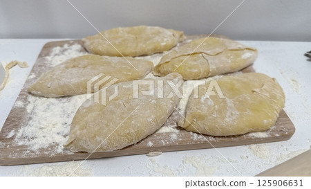 Homemade dough pieces with potato arranged on a wooden board with flour scattered around 125906631