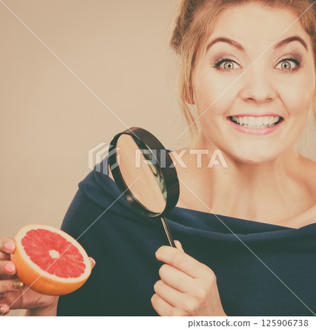 Woman holding magniferlooking grapefruit Woman holding magniferlooking grapefruit 125906738