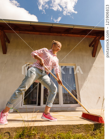 Woman cleaning patio using brush broom 125906813