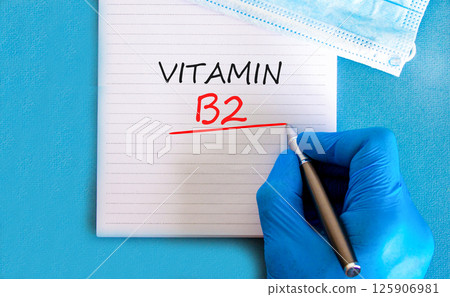 Vitamin B2 riboflavin symbol. Concept words Vitamin B2 on beautiful white note. Doctor's hand in blue medical glove. Beautiful blue background. Medical healthy lifestyle Vitamin B2 riboflavin concept. Vitamin B2 riboflavin symbol. Concept words Vitamin B2 on beautiful white note. Doctor's hand in blue medical glove. Beautiful blue background. Medical healthy lifestyle Vitamin B2 riboflavin concept. 125906981