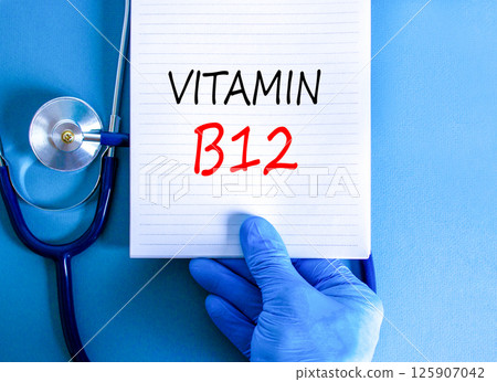 Vitamin B12 symbol. Concept words Vitamin B12 on beautiful white note. Doctor's hand in blue medical glove. Stethoscope. Beautiful blue background. Medical healthy lifestyle Vitamin B12 concept. 125907042