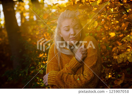 Woman in autumn park warming herself 125907058