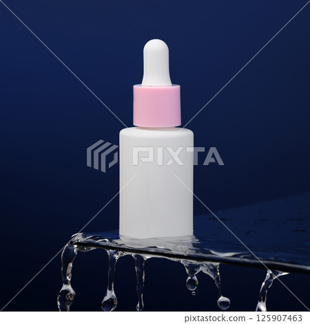In the blue background, a bottle of serum stands on glass. Drops of water drip off the glass. Promotional photo of cosmetics. Mockup. Template.  In the blue background, a bottle of serum stands on glass. Drops of water drip off the glass. Promotional photo of cosmetics. Mockup. Template.  125907463