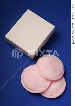 White box and three cotton reusable pink make-up remover pads on a blue background. The concept of ecology and conscious consumption. Reusable disks. White box and three cotton reusable pink make-up remover pads on a blue background. The concept of ecology and conscious consumption. Reusable disks. 125907472