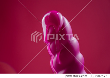 Lube pouring on pink dildo on pink background.  125907576