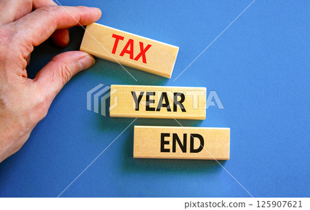 Tax year end symbol. Concept words Tax year end on beautiful wooden blocks. Beautiful blue background. Businessman hand. Business tax year end concept. Copy space. 125907621