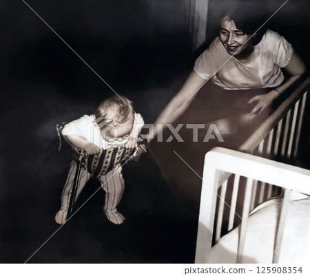 Vintage portrait of a little boy in a walker and his mother. The child is learning to walk. Retro photo from 1967. Vintage portrait of a little boy in a walker and his mother. The child is learning to walk. Retro photo from 1967. 125908354