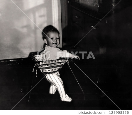 Vintage portrait of little boy in a walker. The child learns to walk. Retro photo 1967. 125908356