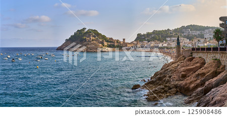 Scenic coastal view of Tossa de Mar, Spain, featuring a beautiful beach, castle, and boats in the sea on a sunny day. 125908486