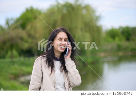 Smiling woman making a video call in park and pointing upward Smiling woman making a video call in park and pointing upward 125908742