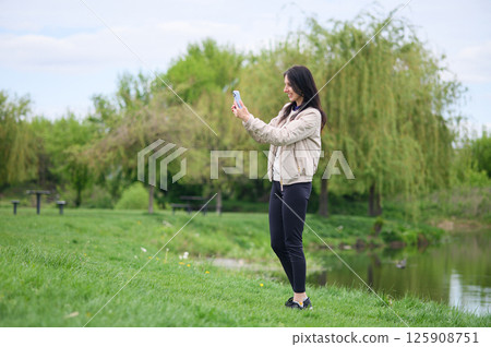 Smiling woman making a video call in park and pointing upward 125908751