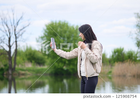 Smiling woman making a video call in park and pointing upward Smiling woman making a video call in park and pointing upward 125908754